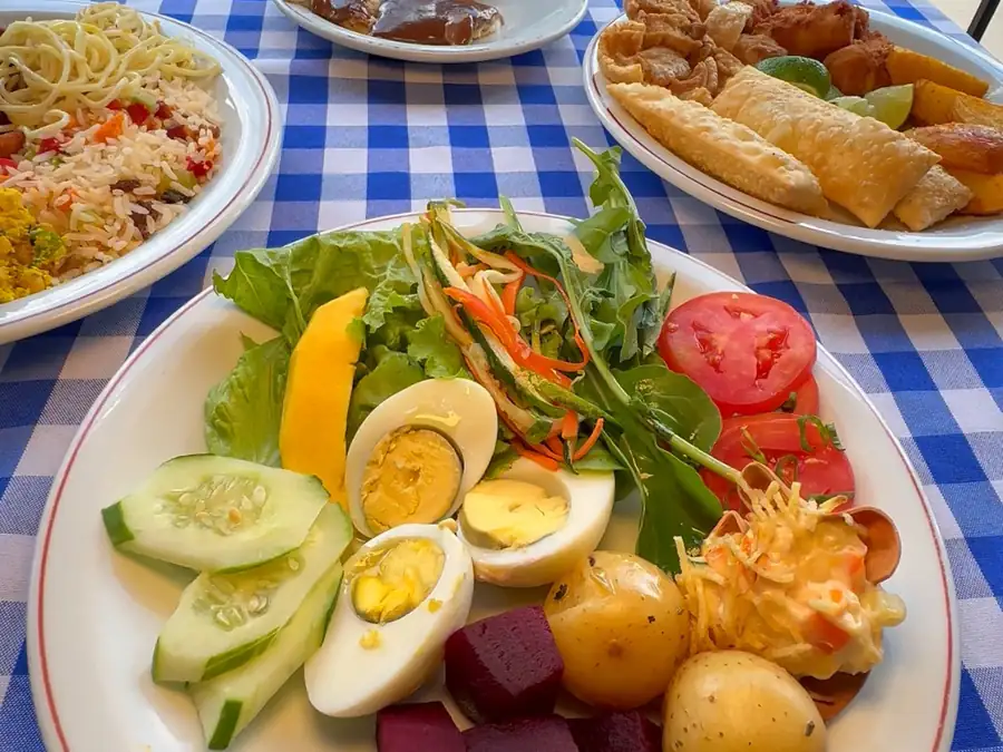 Prato do buffet com salada, ovos, batatas e beterraba, sobre toalha xadrez azul