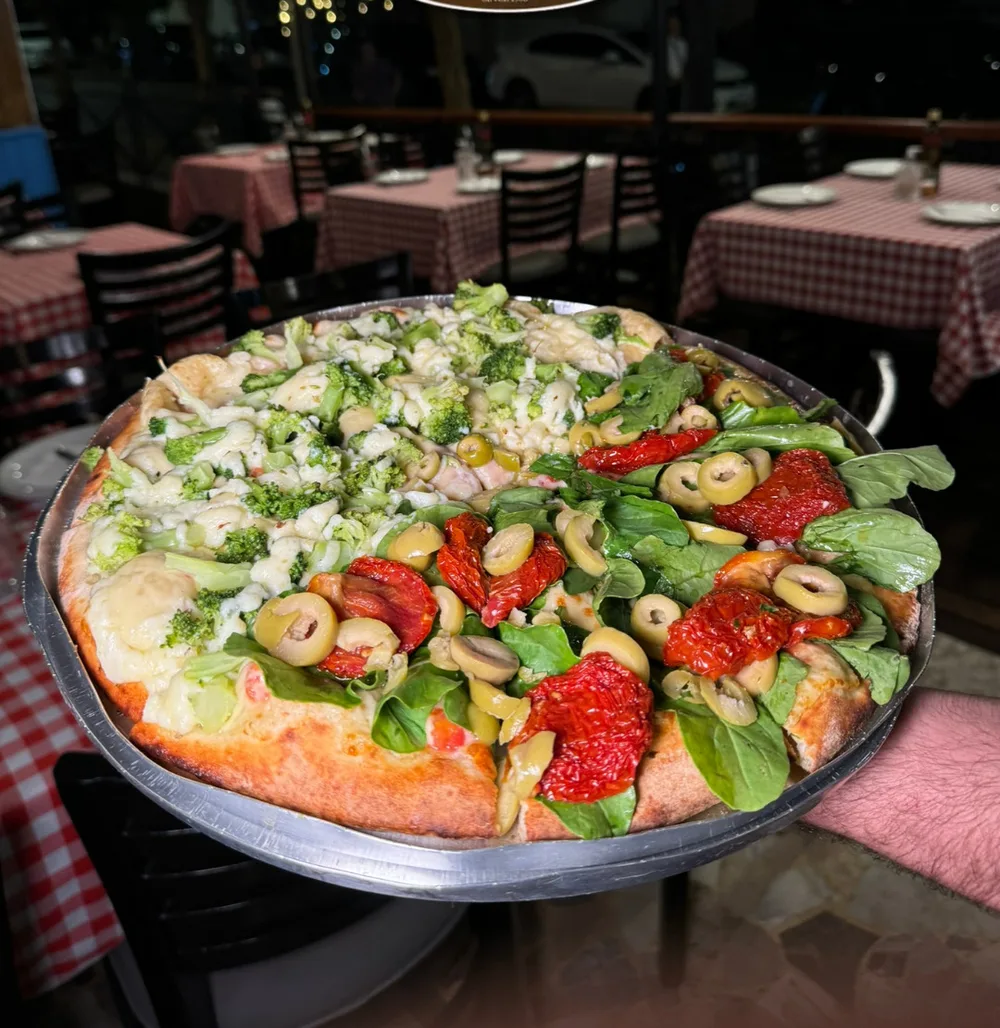 Pizza servida em bandeja, com o salão da unidade Cambuí ao fundo