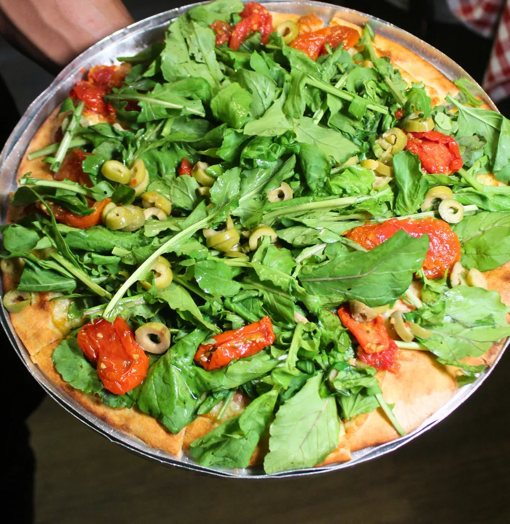 Pizza com cobertura de folhas verdes e tomate, servida em bandeja