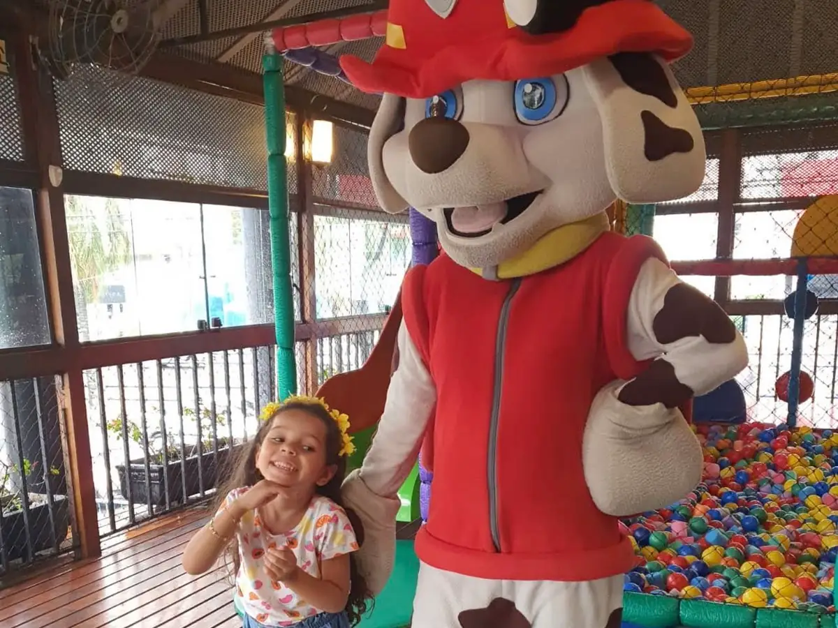 Menina ao lado do mascote de cachorro dálmata vestido de bombeiro, no Espaço Kids